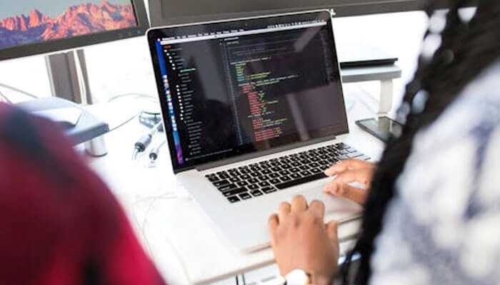 Bigdrop new york developer writing code on a laptop with multiple monitors in a modern workspace.