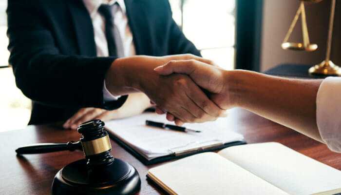 A handshake in a legal setting with a gavel, documents, and scales, symbolizing agreement or collaboration in a civil case.