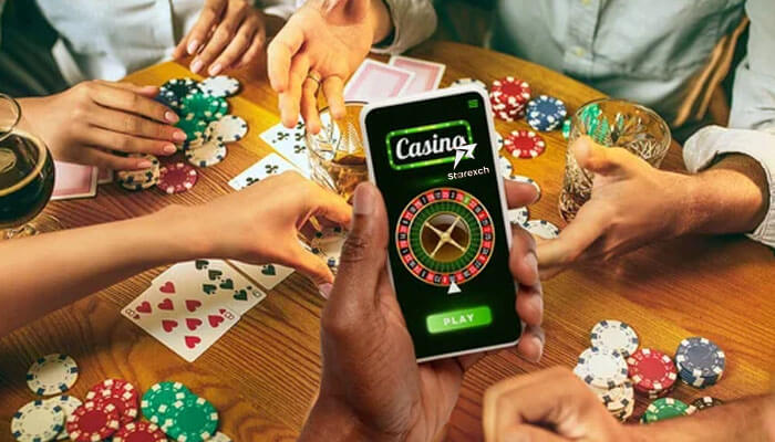 Group playing poker with cards and chips, while one person uses a smartphone displaying the live casino starexch game.