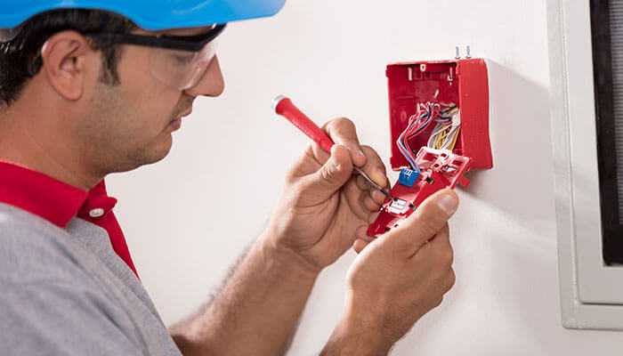 Technician in a blue safety helmet working on the fire alarm system, showing electrical services for home safety.