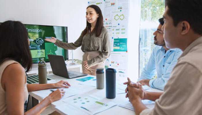 Team collaborating in an office setting presenting data on a screen, illustrating sustainable business transformation strategies.