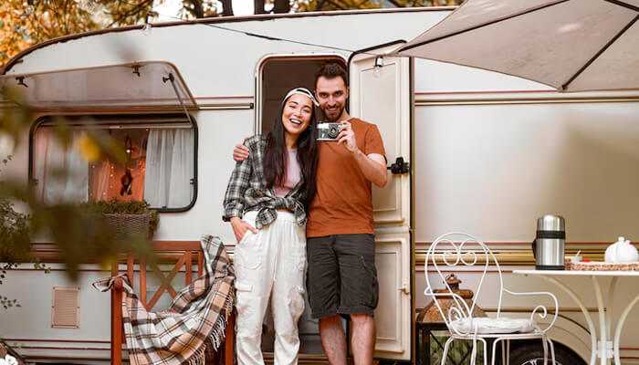 Happy couple posing outside their motorhome set up as a cozy living space, illustrating lifestyle choices that may lead to motorhome insurance exclusions for full-time residence use.