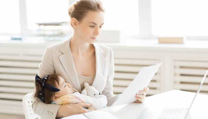 Working mother holding her baby while reading documents at her desk, showing family friendly benefits at work.