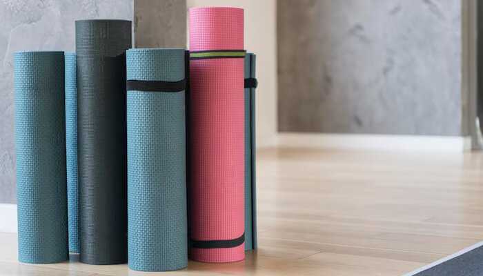 Multiple rolled-up gym floor mats in various colors neatly stored against a wall in a home or studio fitness space.