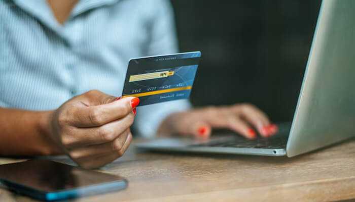 A person holding the hdfc bank millennia credit card while using a laptop for online shopping.