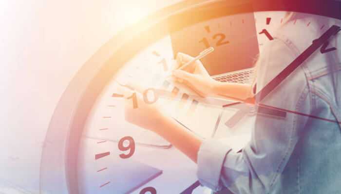 A close-up of a person writing in a notebook with a large clock superimposed, symbolizing time management and productivity, to overcome procrastinate.