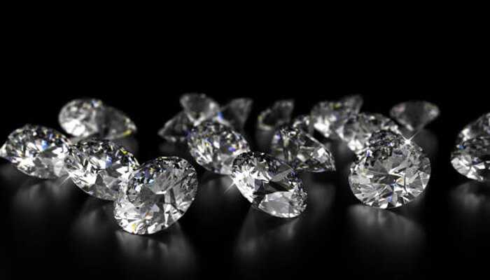 Multiple oval-cut color diamonds sparkling under spotlight on a black background, showcasing contrast and clarity differences.