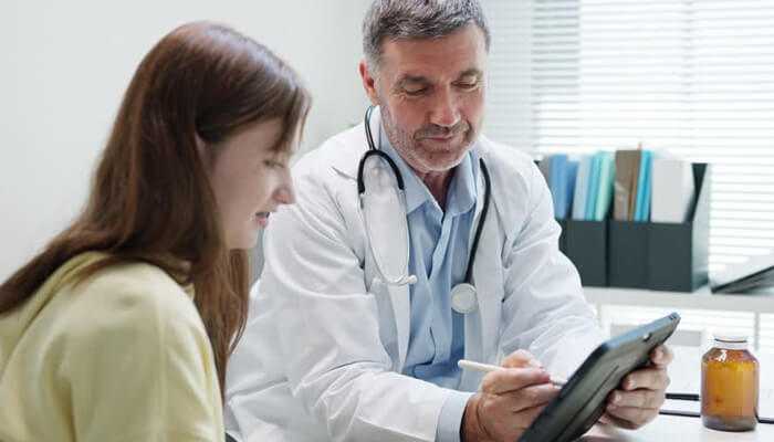 A doctor and patient discussing health insurance options, possibly related to west virginia health insurance, with a digital tablet in the doctor's hand showing relevant information.
