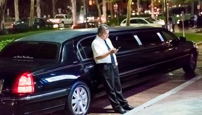 Chauffeur waiting beside black limousine during a night event — ideal representation for limousine booking experience.