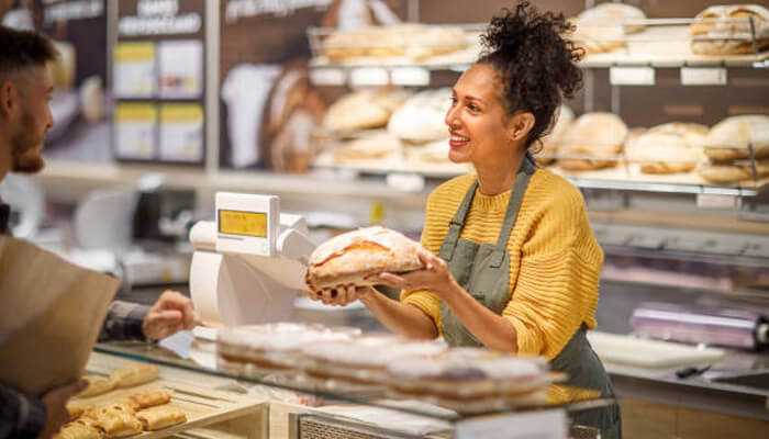 Female bakery owner smiling while serving a customer, representing the spirit of local entrepreneurship in community-focused businesses.