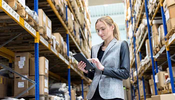 Businesswoman managing inventory in warehouse using tablet, illustrating sourcing through online distributors and order management.