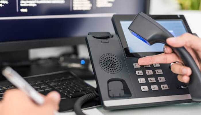 Voip security in business communication: close-up of a person dialing on a voip office phone next to a computer screen