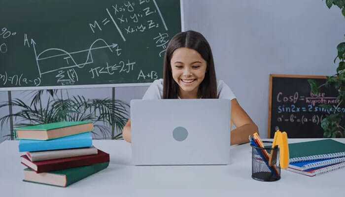 Uplarn. Com: a smiling student working on a laptop in a study environment, surrounded by books and stationery, with a blackboard full of mathematical equations in the background.