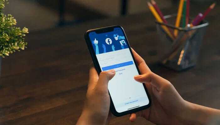 Close-up of a hand holding a phone displaying the facebook login screen, demonstrating how to restrict someone on facebook.